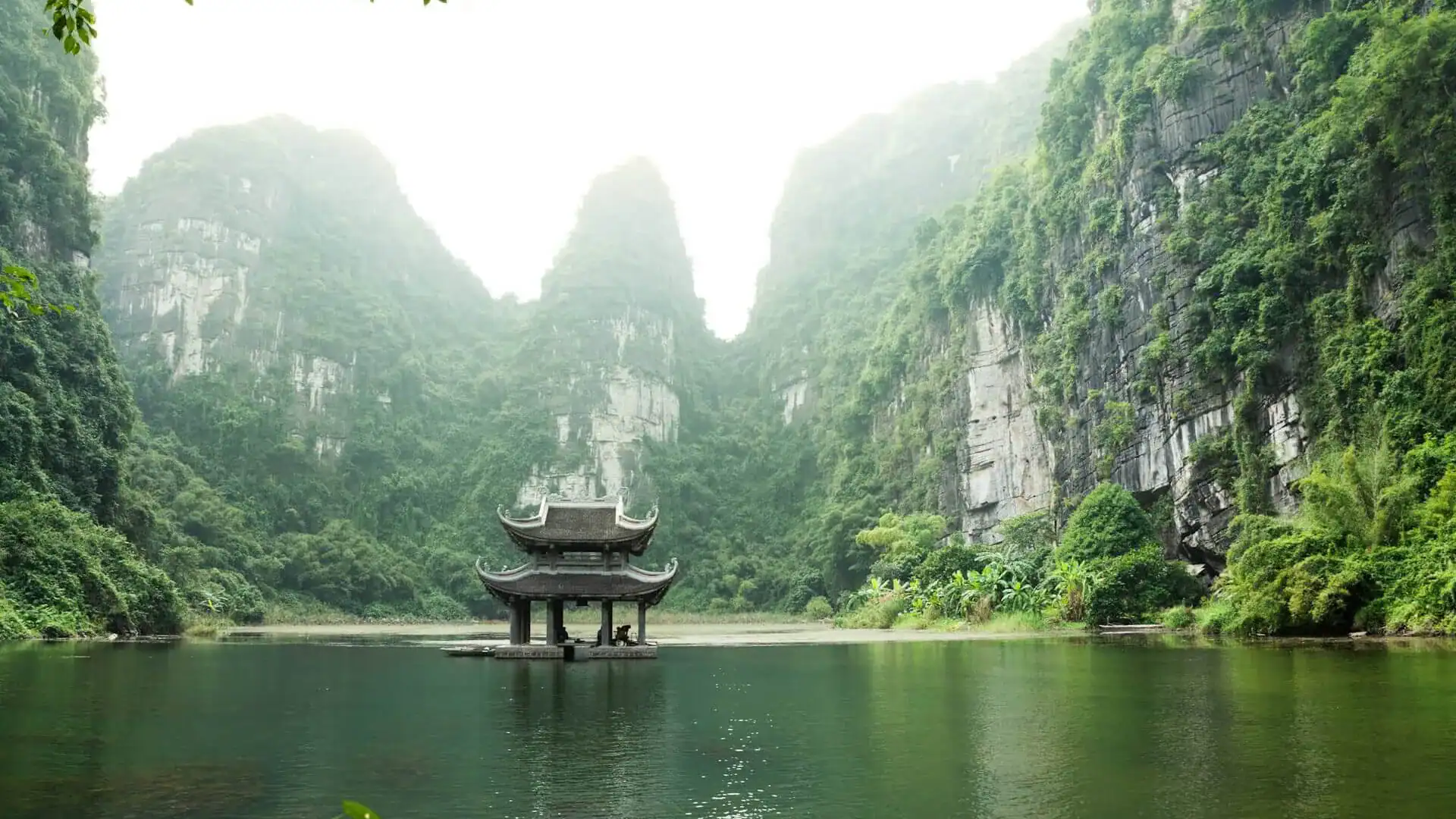 En liten byggnad vid vattnet med berg i bakgrunden i Vietnam.